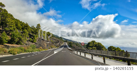 Scenic winding road through lush green hills under a bright blue sky with fluffy white clouds, showcasing a tranquil landscape in a mountainous volcanic region. High quality photo Scenic winding road through lush green hills under a bright blue sky with fluffy white clouds, showcasing a tranquil landscape in a mountainous volcanic region. High quality photo 140265155