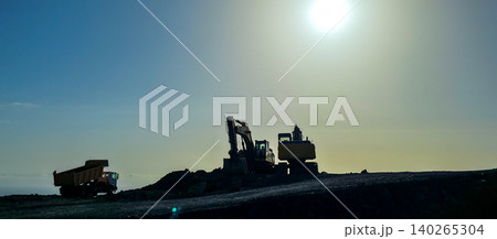 Specialized equipment machine with hydraulic arm positioned on volcanic rock and solidified lava overlooking the ocean under a clear blue sky with distant mountains visible. High quality photo 140265304
