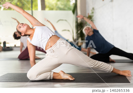 Group of sporty women practicing various yoga positions during training indoors, focus on young female Group of sporty women practicing various yoga positions during training indoors, focus on young female 140265336