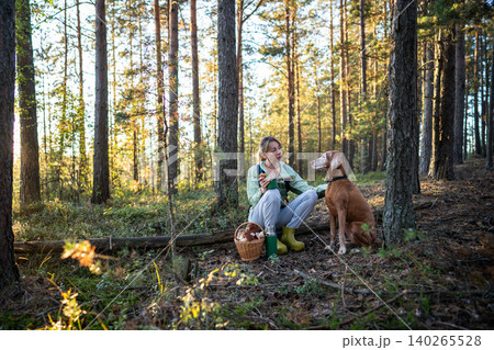 Woman forager petting Vizsla dog and speaking calmly on forest break after mushroom hunt Woman forager petting Vizsla dog and speaking calmly on forest break after mushroom hunt 140265528