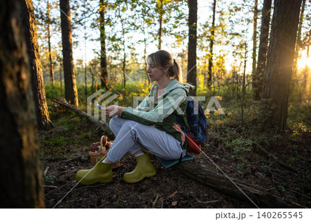 Engaged female forager photographing mushrooms in basket with smartphone on forest clearing 140265545