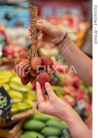 Woman choosing ripe lychee fruits at supermarket in Thailand, holding bunch of fruits on branches. 140265552