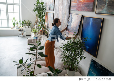 Talented woman painter hanging new finished artwork canvas on wall at home loft gallery studio. 140265706