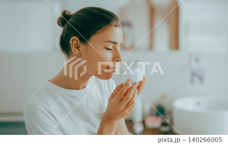Young Caucasian adult woman smelling organic cream jar in bright sunny home bathroom Young Caucasian adult woman smelling organic cream jar in bright sunny home bathroom 140266005