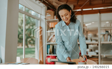 Middle aged Hispanic woman smiling and adjusting a wooden chair in a bright modern office Middle aged Hispanic woman smiling and adjusting a wooden chair in a bright modern office 140266015