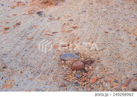 Small stones and orange clay fragments on sandy road surface, close-up texture of rural dirt pathway ground Small stones and orange clay fragments on sandy road surface, close-up texture of rural dirt pathway ground 140266062