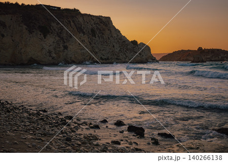 rocky pebble beach foreground with soft ocean waves approaching massive cliffs during golden hour rocky pebble beach foreground with soft ocean waves approaching massive cliffs during golden hour 140266138