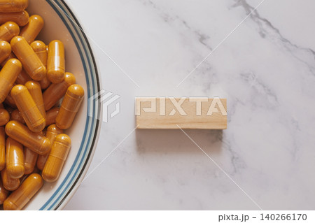 Natural curcumin capsules on marble and wood, showcasing clean eco-friendly wellness aesthetics with bright botanical supplements for modern biohacking and minimalist health visuals 140266170