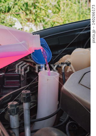 Process of pouring pink windshield washer fluid from a plastic canister into the reservoir tank under an open car hood during regular vehicle maintenance service Process of pouring pink windshield washer fluid from a plastic canister into the reservoir tank under an open car hood during regular vehicle maintenance service 140266173