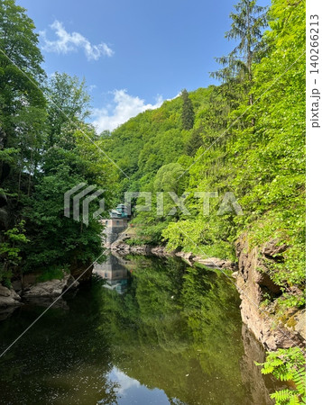 Scenic river surrounded by lush green trees and rocky cliffs in nature 140266213