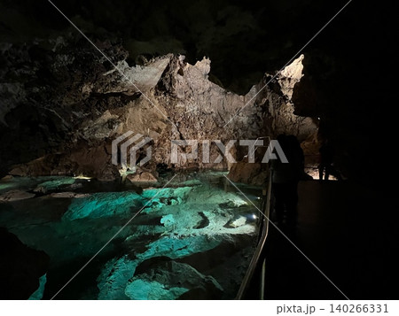 Underground cave with illuminated water and rock formations in darkness 140266331