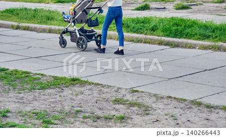 Legs in jeans of young mother walking with baby stroller Legs in jeans of young mother walking with baby stroller 140266443