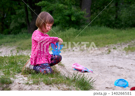 Little girl in red dress playing with toys on sand on nature 140266581