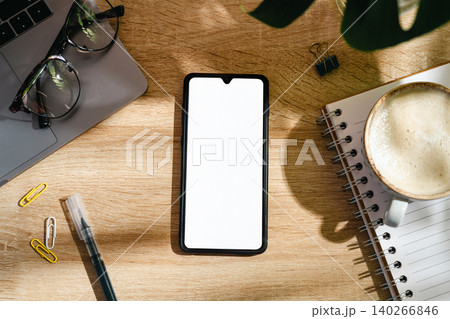 Blank smartphone screen mockup on home office desk with coffee and notebook, top view workspace Blank smartphone screen mockup on home office desk with coffee and notebook, top view workspace 140266846