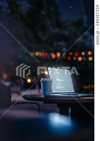 Working on a laptop at night in an outdoor setting with lights in the background 140267354