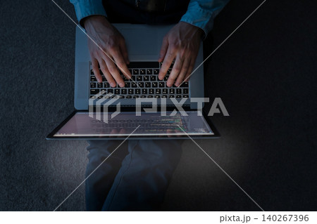 Person types on laptop while seated in a dimly lit room during evening hours Person types on laptop while seated in a dimly lit room during evening hours 140267396