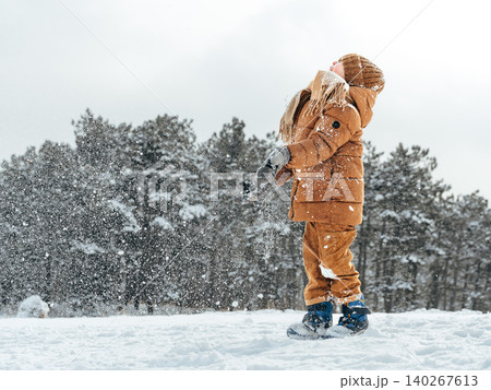 Child plays in snow while wearing warm clothes and enjoying a winter day outdoors 140267613
