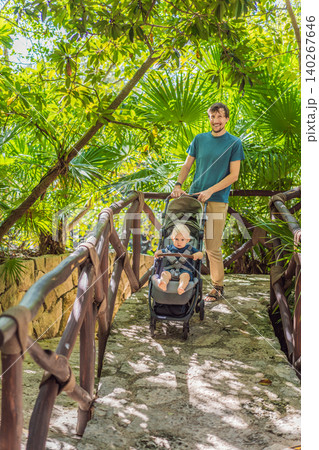 Dad walks with an infant stroller through dense tropical greenery, showing family travel, fatherhood, eco park visit and vacation routine concept 140267646