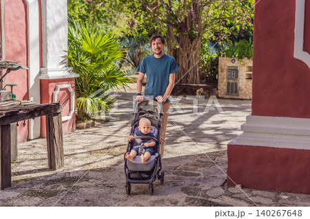 Man walking with baby stroller through Mexican colonial street, colorful architecture, heritage courtyard, fatherhood and family travel with baby concept 140267648