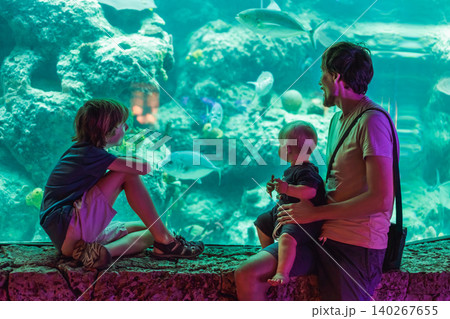Father with two sons watching underwater world at large aquarium window, family bonding, marine life education and travel with kids concept 140267655