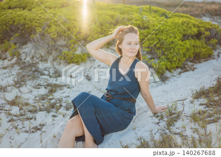 Female traveler relaxes among coastal plants and white sand dunes with ocean view, showing calm summer travel, wellness and beach lifestyle concept 140267688