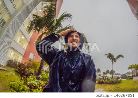 Adult man faces heavy rain and strong wind near palm trees and city buildings, showing storm weather, hurricane season and climate resilience concept Adult man faces heavy rain and strong wind near palm trees and city buildings, showing storm weather, hurricane season and climate resilience concept 140267851