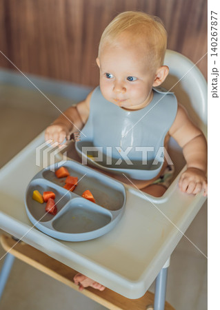 Infant practices self feeding with vegetables in a kitchen, showing baby led weaning, early nutrition and family care concept Infant practices self feeding with vegetables in a kitchen, showing baby led weaning, early nutrition and family care concept 140267877