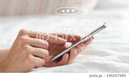 Person sending a text message on a phone while sitting on a bed during the day 140267980