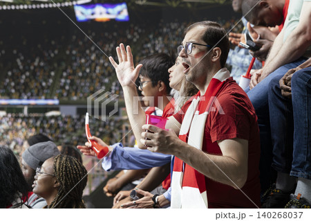 Tense football supporters reacting to a dramatic final minute attack during live soccer match in crowded stadium stands with scarf and vuvuzela energy. Anticipation dominate the decisive moment. Tense football supporters reacting to a dramatic final minute attack during live soccer match in crowded stadium stands with scarf and vuvuzela energy. Anticipation dominate the decisive moment. 140268037