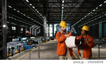 Diverse team of engineers studying blueprints and layout plans in machinery hall, man and woman checking instructions and circuits for heavy equipment to ensure production workflow. Diverse team of engineers studying blueprints and layout plans in machinery hall, man and woman checking instructions and circuits for heavy equipment to ensure production workflow. 140268056