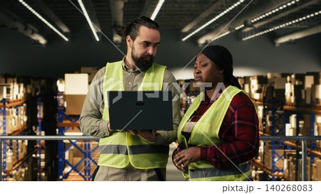 Multiethnic employees managing warehouse operations on laptop software, industrial job on platform. Wearing high visibility vest, worker oversees inventory and parcel shipment, workflow control. Multiethnic employees managing warehouse operations on laptop software, industrial job on platform. Wearing high visibility vest, worker oversees inventory and parcel shipment, workflow control. 140268083