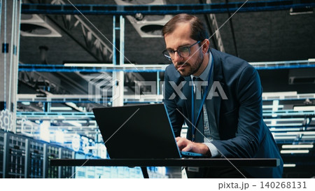 Data center admin typing on laptop keyboard, doing resource optimization using software. Server farm IT specialist using notebook program to upgrade hardware supercomputers, camera A Data center admin typing on laptop keyboard, doing resource optimization using software. Server farm IT specialist using notebook program to upgrade hardware supercomputers, camera A 140268131
