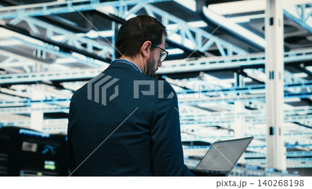 Software developer in data center using laptop to code, managing rigs powering online platforms. Server room employee doing checkup on systems using programming script on notebook Software developer in data center using laptop to code, managing rigs powering online platforms. Server room employee doing checkup on systems using programming script on notebook 140268198