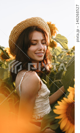 Woman enjoying a sunny day in a field of sunflowers while wearing a straw hat Woman enjoying a sunny day in a field of sunflowers while wearing a straw hat 140268527