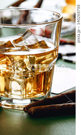 Glass of whiskey with ice and cigars on a table with other items in background 140268788