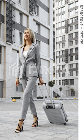 Woman walking with suitcase in urban area during daytime near modern buildings 140268828
