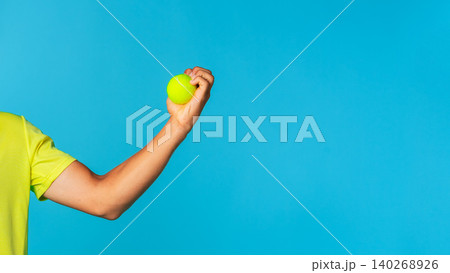 Person holds a green tennis ball against a blue background near a bright light source Person holds a green tennis ball against a blue background near a bright light source 140268926