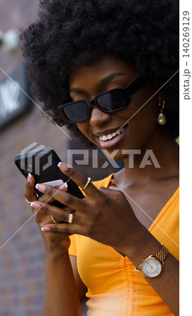 Woman smiles while using smartphone outside on a sunny day in urban setting Woman smiles while using smartphone outside on a sunny day in urban setting 140269129