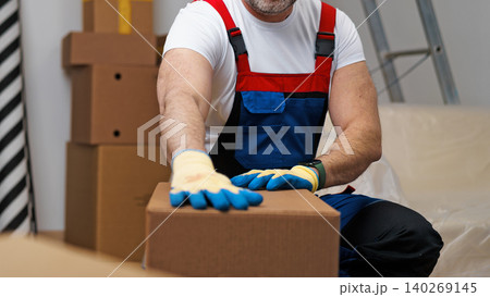 Worker in blue and red outfit moves cardboard box in storage area Worker in blue and red outfit moves cardboard box in storage area 140269145
