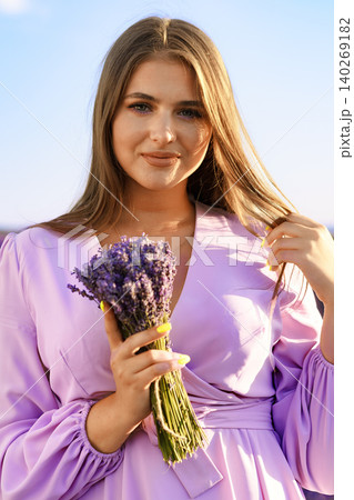 Young woman holds lavender flowers by the sea in a sunny outdoor setting during the day 140269182