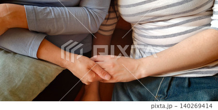 Sincere moments between a mother and teenage daughter holding hands, showcasing their connection while seated on a couch in a cozy indoor setting 140269414