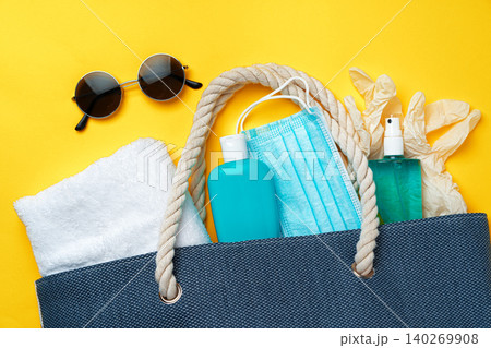 Blue beach bag with beach accessories and protective mask on yellow background 140269908