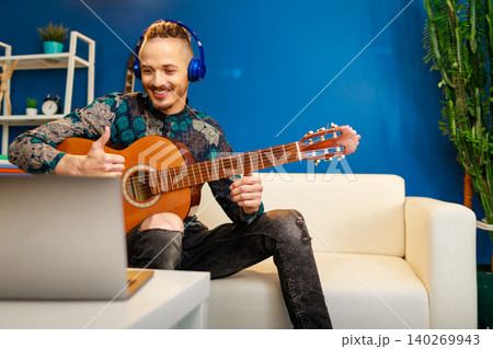 Young stylish caucasian man taking guitar class online at home using his laptop Young stylish caucasian man taking guitar class online at home using his laptop 140269943