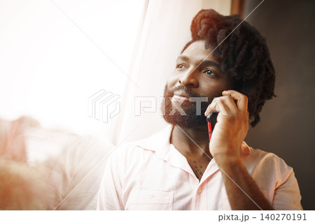 Close up photo of a black man in formal shirt talking on his phone near the window Close up photo of a black man in formal shirt talking on his phone near the window 140270191