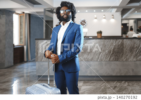Black businessman with packed luggage standing in hotel lobby 140270192