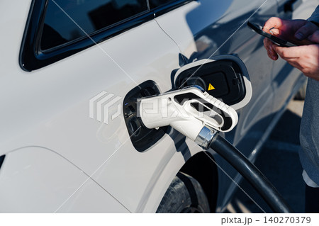 Charging an electric car with an EV charger at a public station during the day Charging an electric car with an EV charger at a public station during the day 140270379