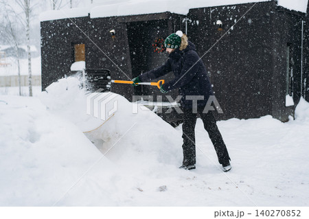 man shoveling snow with a spade on the driveway of his countryside property during a snowfall 140270852