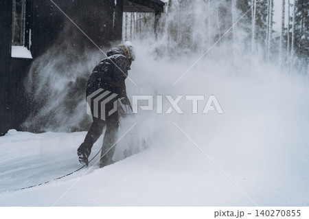 unrecognizable man clearing snowdrifts in countryside by the wooden house using electric snow blower unrecognizable man clearing snowdrifts in countryside by the wooden house using electric snow blower 140270855