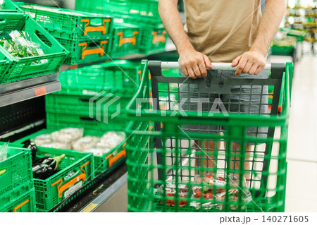Man pushing shopping cart through supermarket produce section, customer buying fresh vegetables and groceries in modern retail store Man pushing shopping cart through supermarket produce section, customer buying fresh vegetables and groceries in modern retail store 140271605