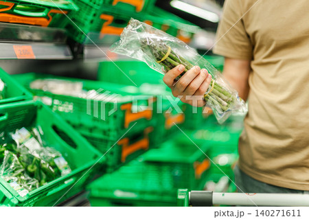 Man choosing fresh asparagus in supermarket produce section, customer selecting healthy vegetables and buying groceries in modern retail store Man choosing fresh asparagus in supermarket produce section, customer selecting healthy vegetables and buying groceries in modern retail store 140271611